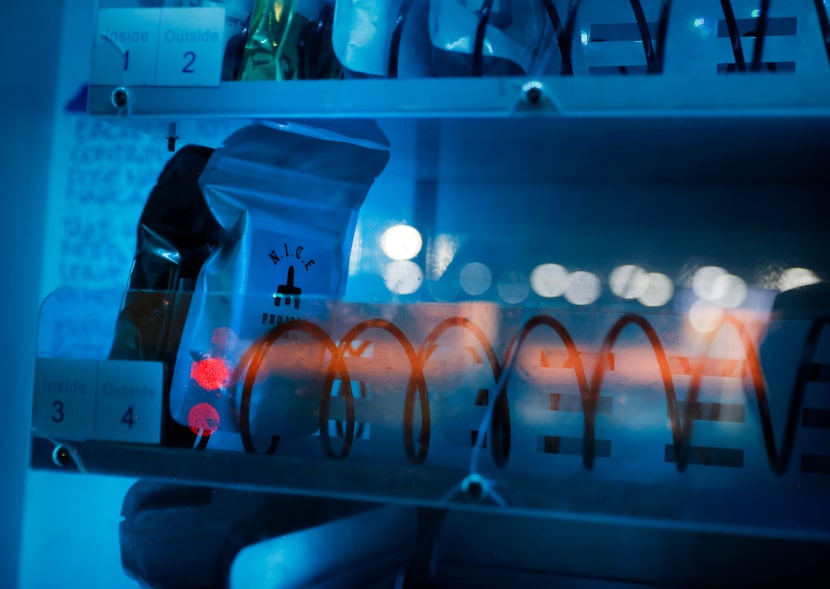 The blue glow of a N.I.C.E. vending machine shows people at the Sunrise Homeless Navigation...