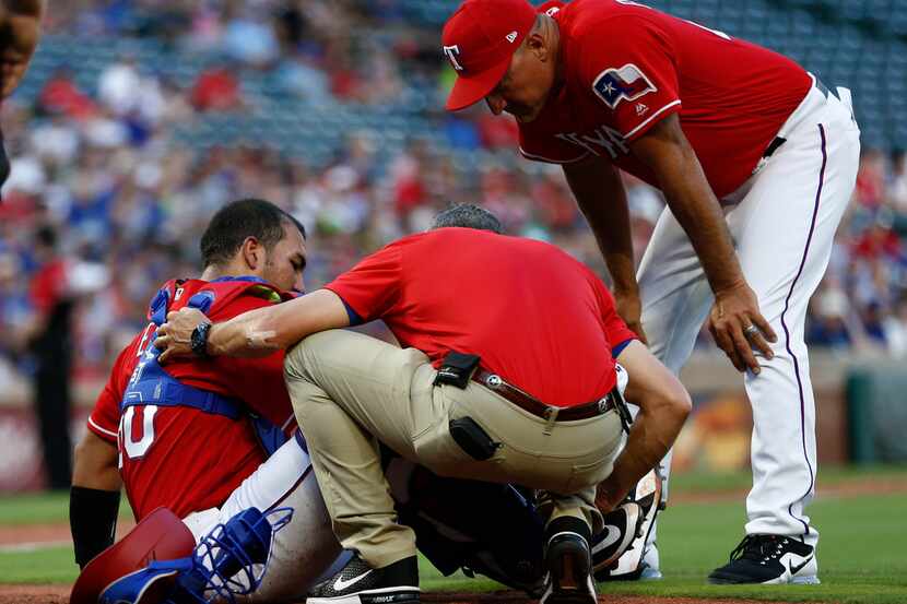 Texas Rangers catcher Carlos Perez, left, is checked by team trainer Kevin Harmon and...