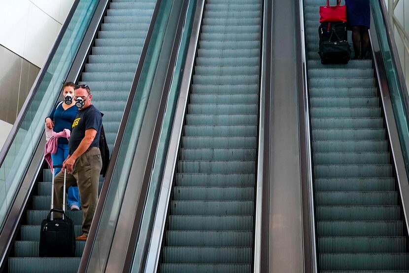 Passengers wearing face masks due to the new coronavirus rode an escalator at DFW...