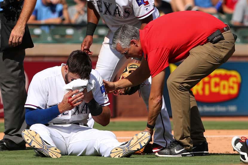 Texas Rangers third baseman Joey Gallo (13) holds a towel to his nose as he is attended by...