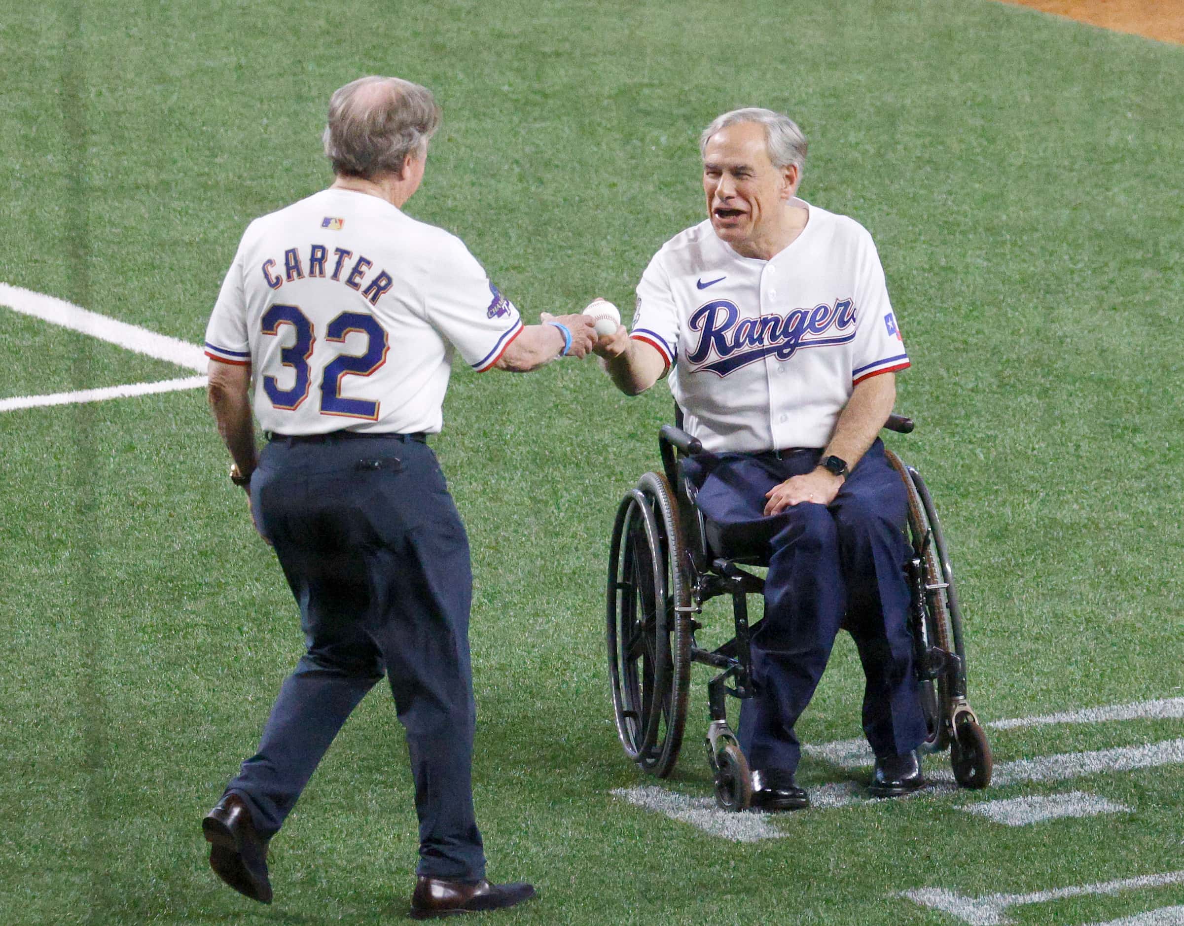 Texas Gov. Greg Abbott, right, hands the ceremonial first pitch baseball to Texas Rangers...