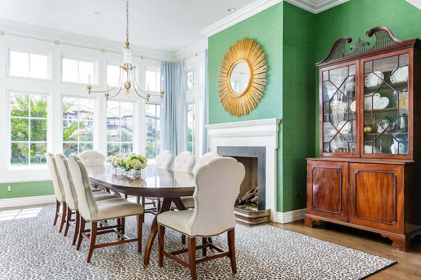 A dining room with green wallpaper has a starburst mirror above the fireplace.
