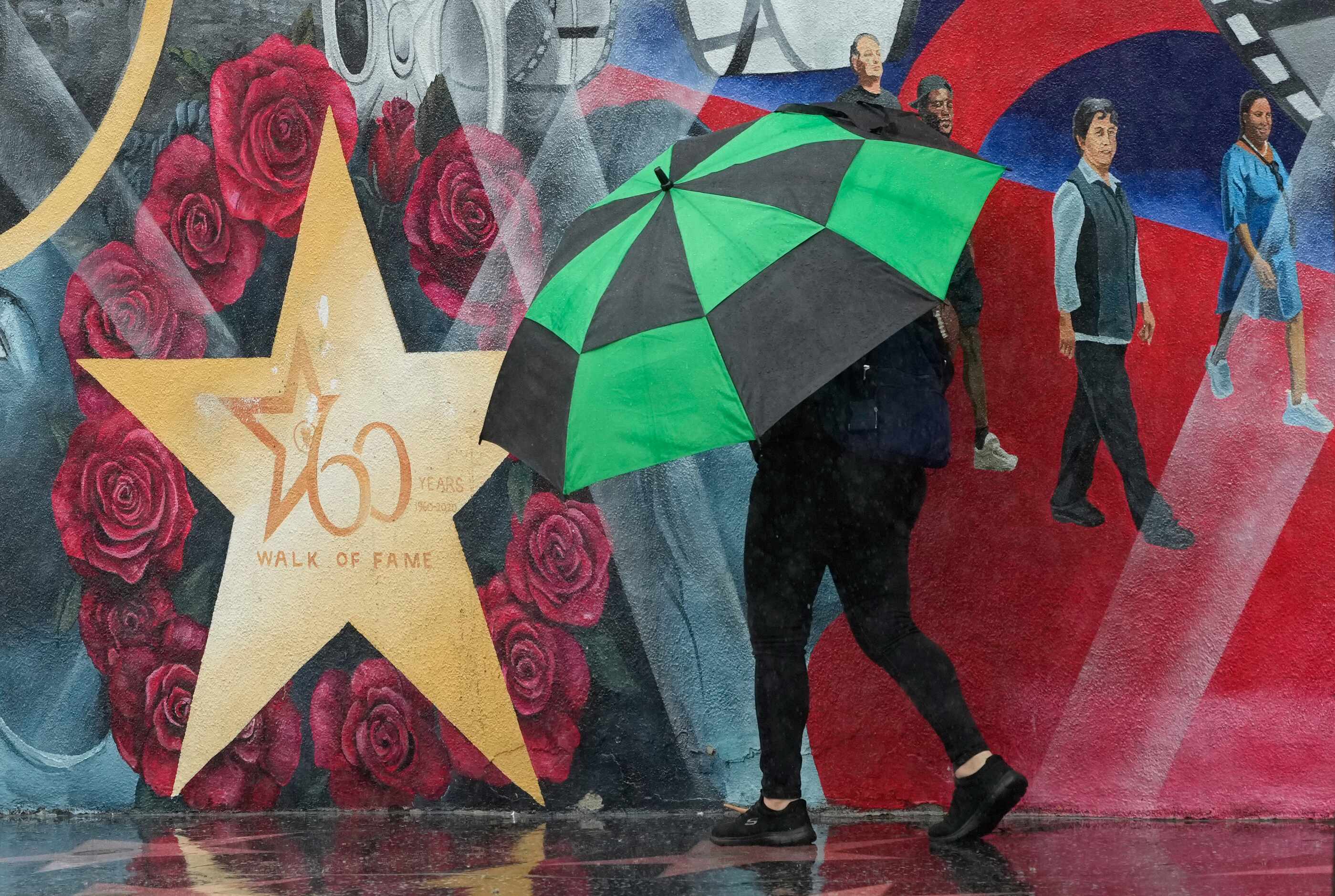 A pedestrian uses an umbrella to shield himself from wind and rain on the Hollywood Walk of...