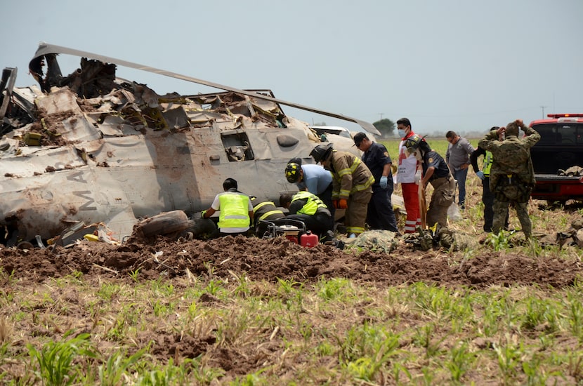 Emergency personnel work next to a navy Blackhawk helicopter crashed after supporting those...