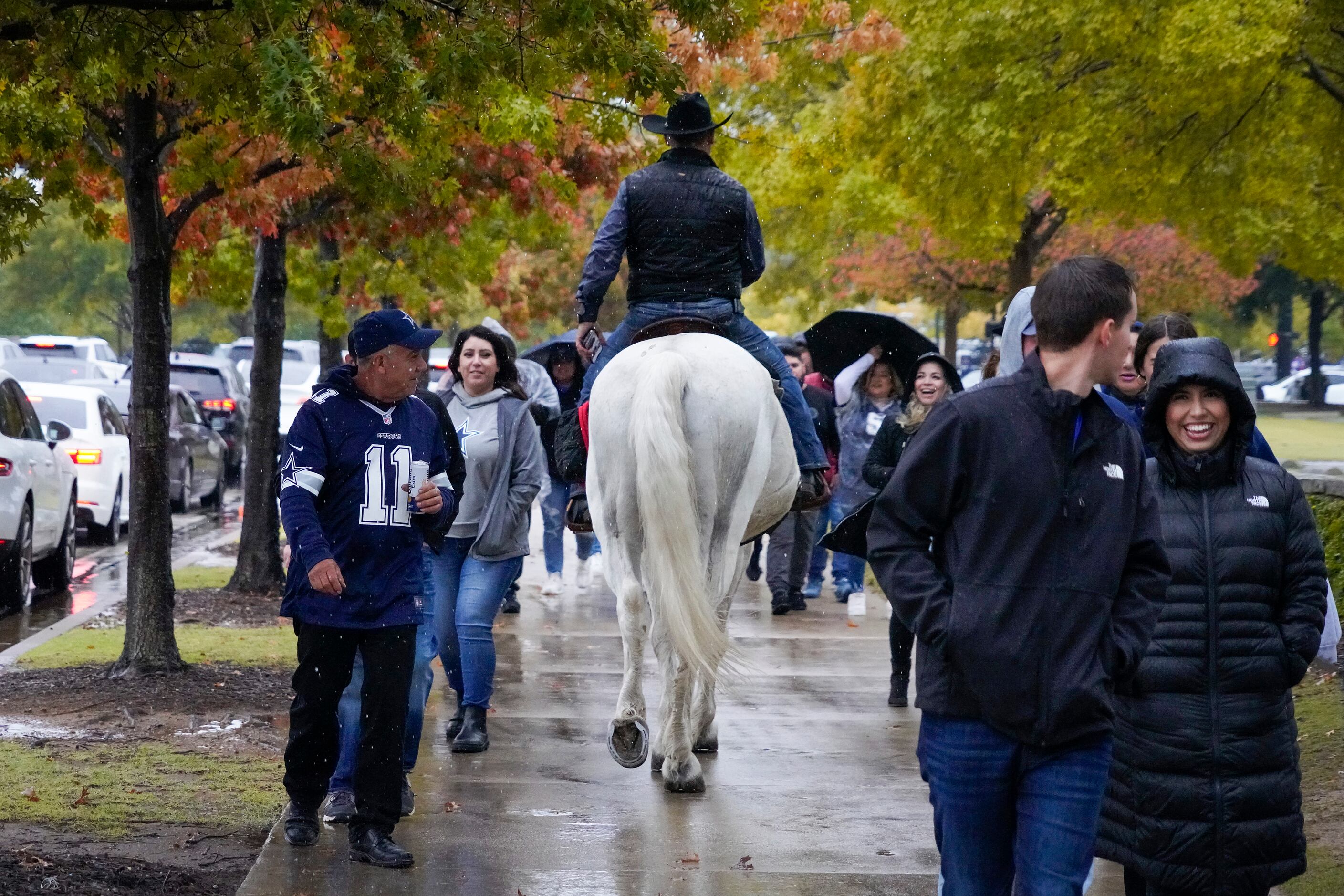 Fans head to the stadium in the rain as a man rides a horse down a sidewalk before an NFL...