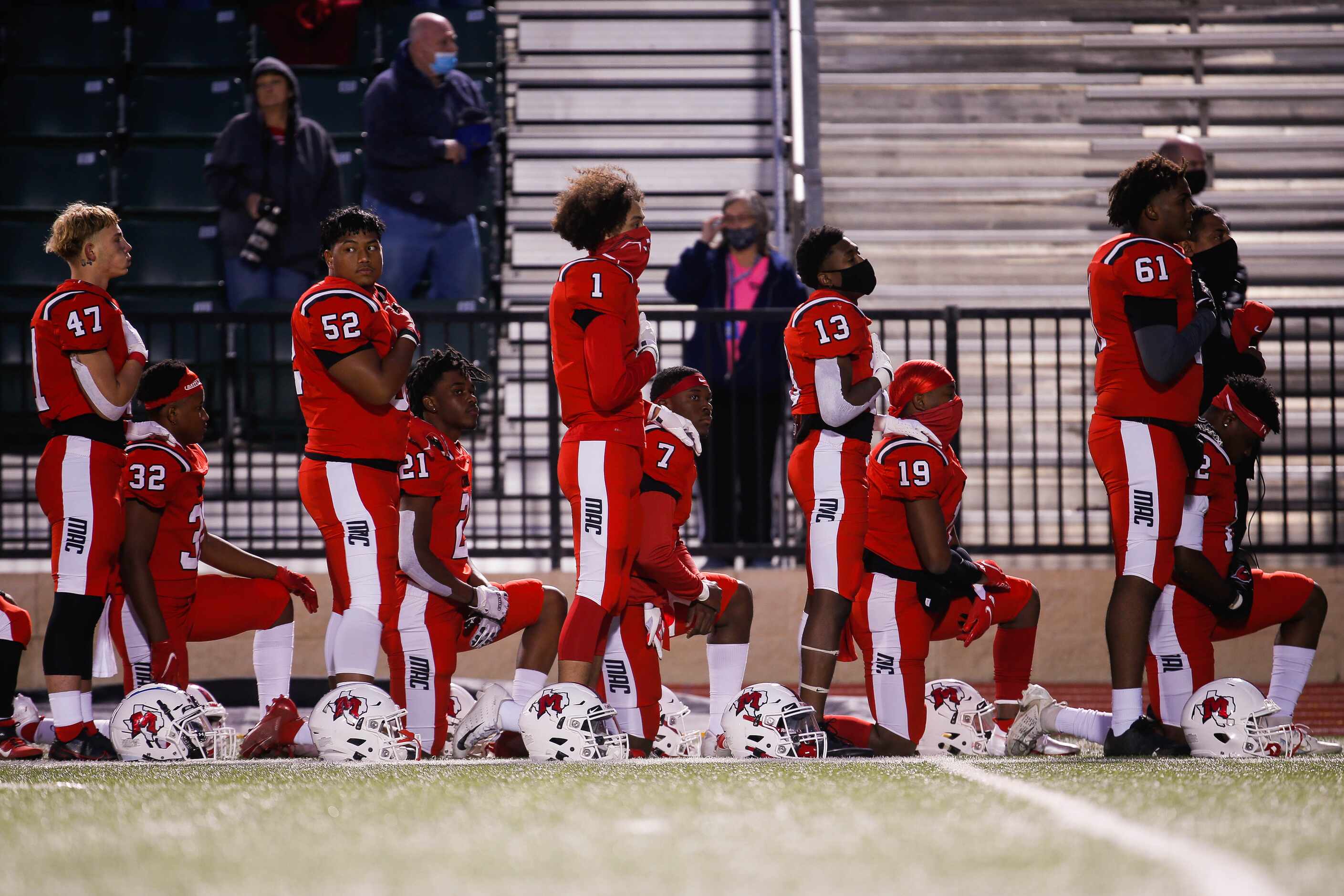 Irving MacArthur High School players kneel and stand during the national anthem before a...