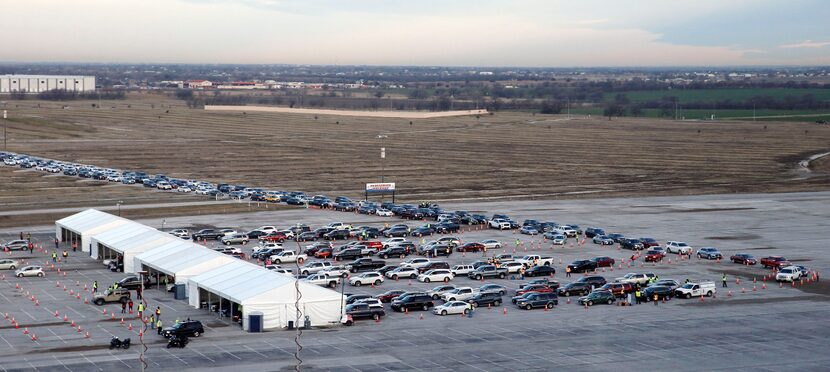 Vehicles make their way through multiple stations at a COVID-19 drive-through vaccination...