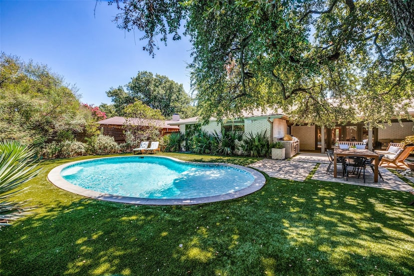 The pool is surrounded by a turfed lawn, covered patio and outdoor kitchen.