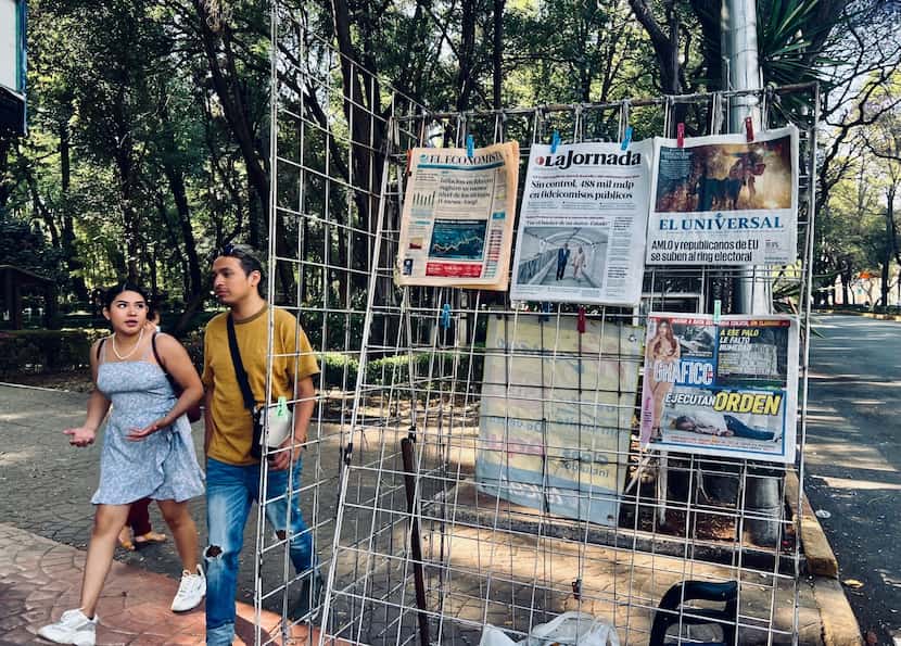 Bystanders walk by a newspaper rack in Mexico City's Parque Mexico. Many of the headlines...