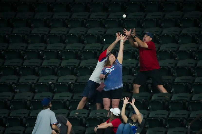 Fans reach for a ball tossed to the crowd by Texas Rangers pitcher José Leclerc during...