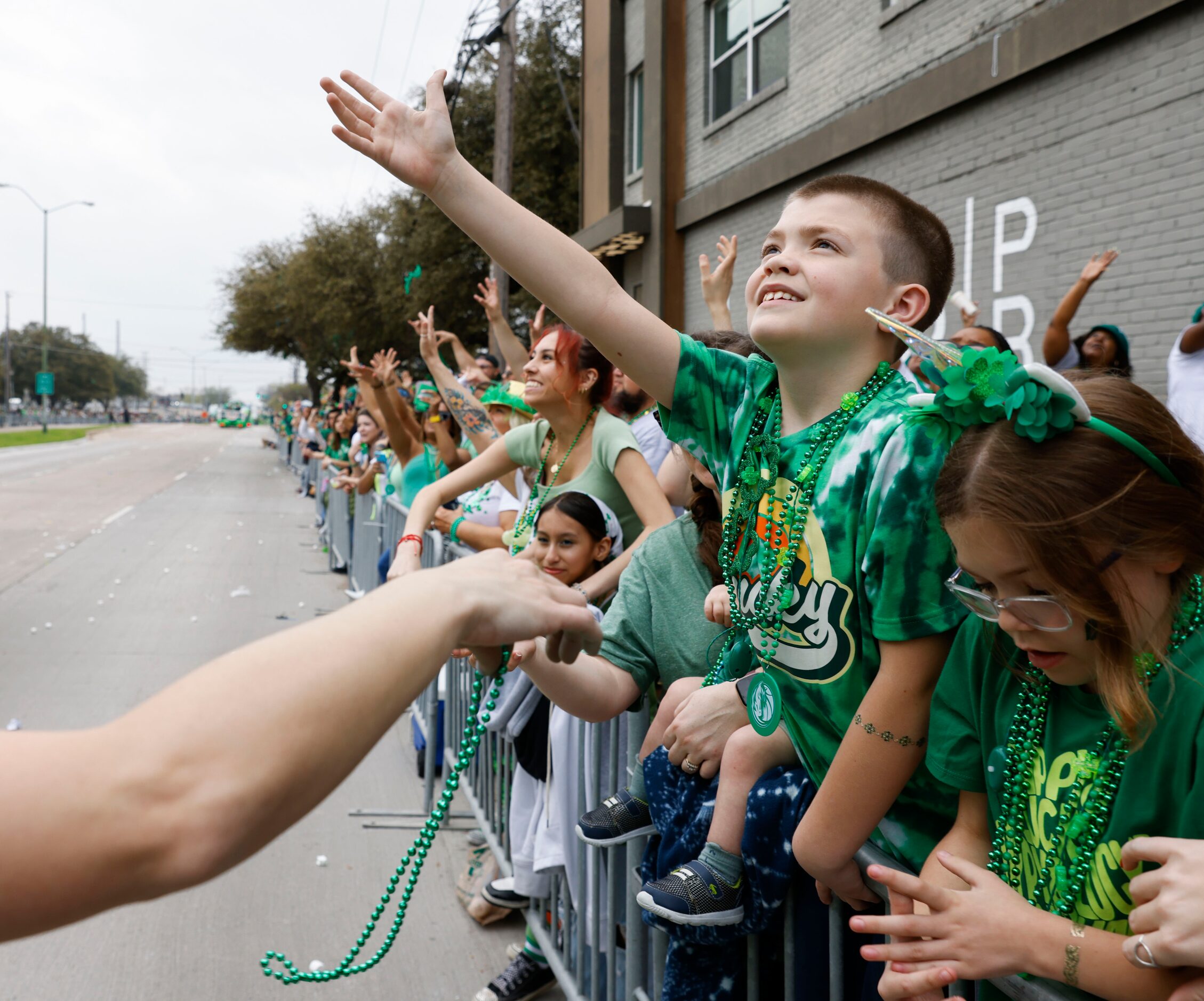 Attending crowd tries to catch green bead necklaces tossed by marchers during a Saint...