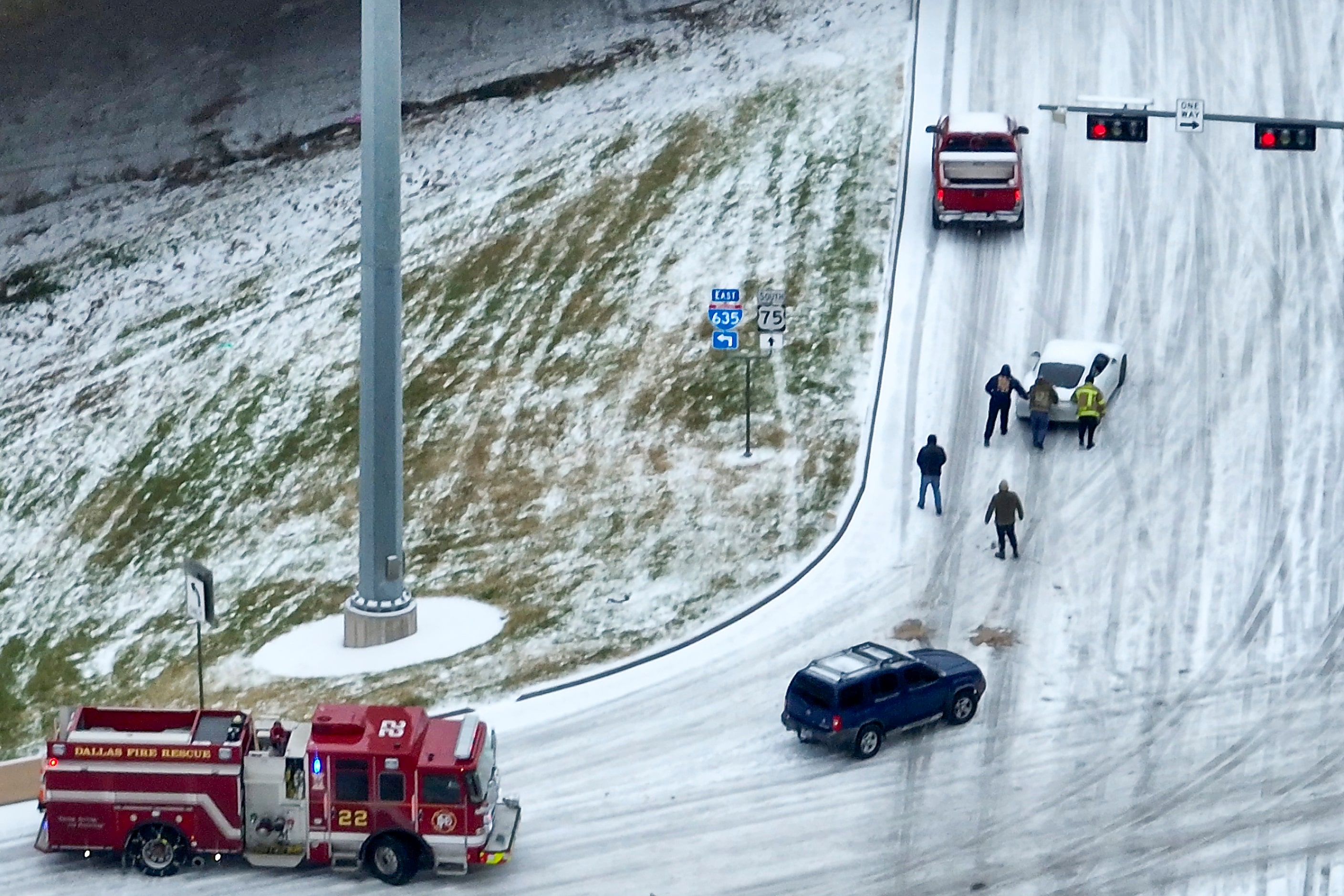 Bystanders and Dallas Fire Rescue personnel push a vehicle as an icy mix covers the High...