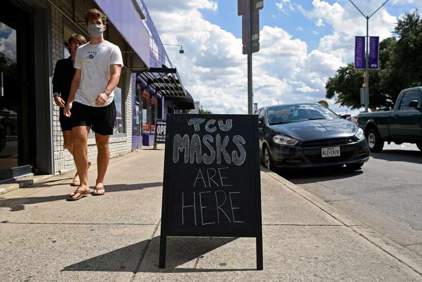 Texas Christian University students walk by signage for masks outside of Flash The...