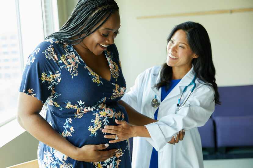 A pregnant woman and her doctor smile as they touch the woman's belly.