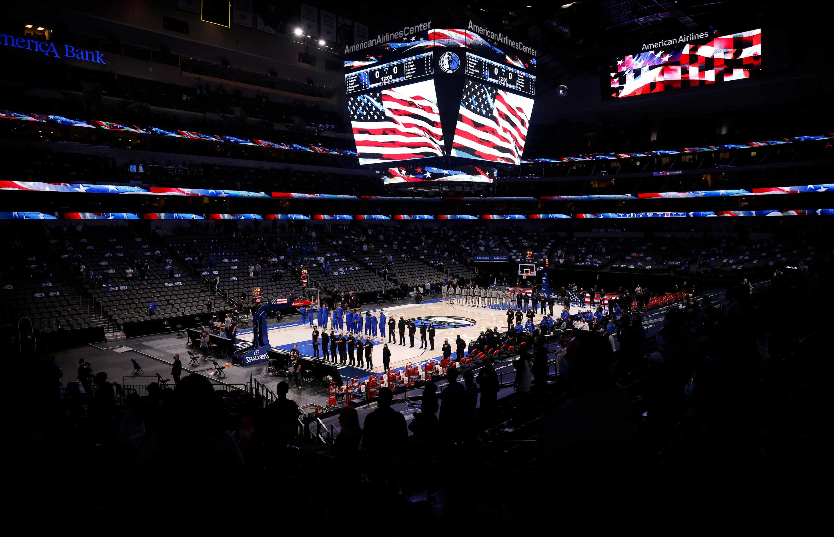 The Dallas Mavericks and Detroit Pistons basketball teams stand and face the flag for the...
