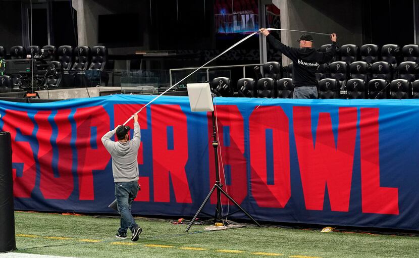 Workers use a tape measure as they hang a sign Jan. 29 inside Mercedes-Benz Stadium for...