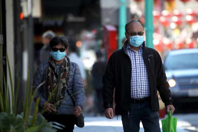 People wear surgical masks as they walk along Chinatown's Grant Avenue on Wednesday in San...