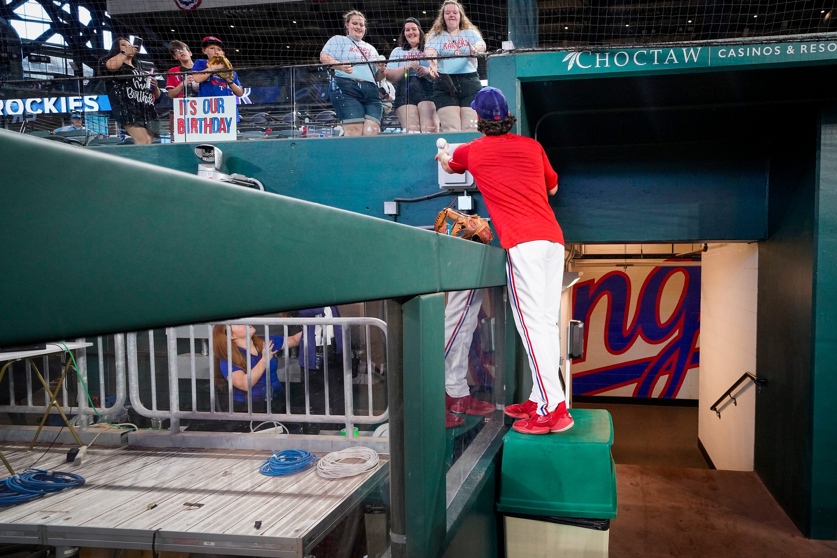 Texas Rangers infielder Charlie Culberson stands on a trash can to toss a ball to fans while...