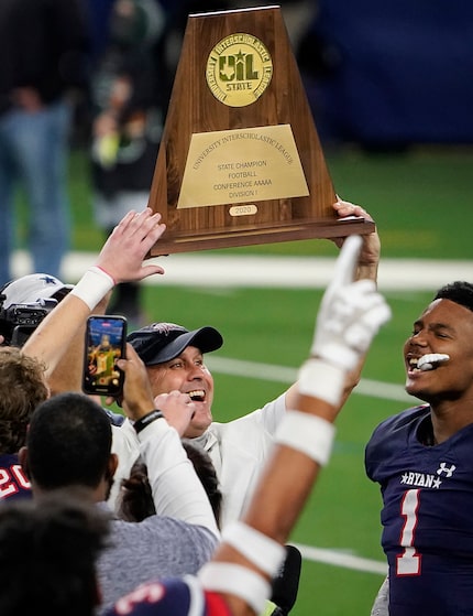 Denton Ryan head coach Dave Henigan lifts the championship trophy as the Raiders celebrate a...