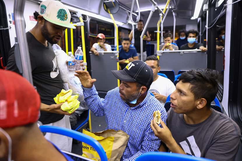 Migrantes comparten comida mientras cargan un autobús que los llevará a un centro de...