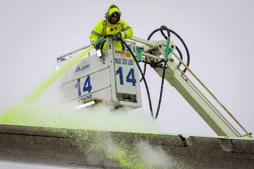 American Airlines worker Gus Rodriquez sprays de-icing solution onto a plane's wing from a...
