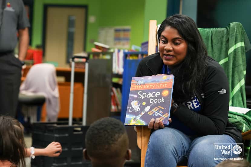 A volunteer shows schoolchildren the cover of a book about space during a Reading Day event.