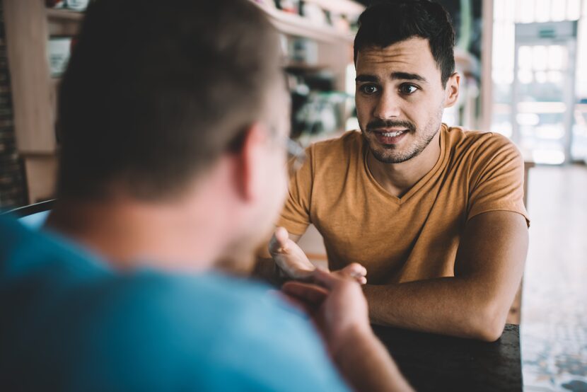 Serious male colleagues have a conversation; one wears an orange shirt and another wears a...