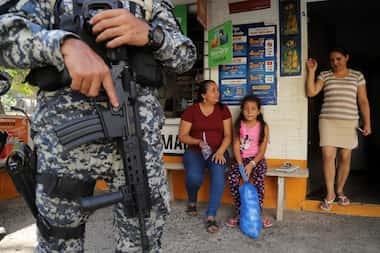 Several people sit at the entrance of a store guarded by a military man in San Antonio Los...