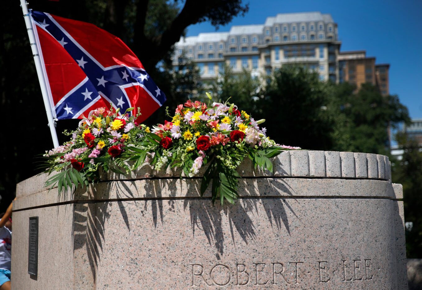 A Confederate flag flies over bouquets of flowers  placed on the Robert E. Lee statue base...