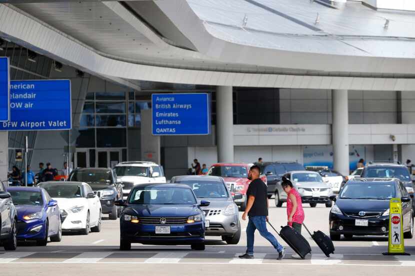 Airline passengers walk across a congested drop-off and pick up area at Dallas-Fort Worth...