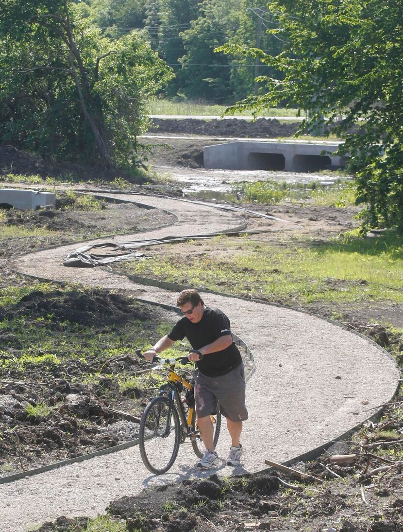 
Gordon Porter walks his bike on a soft rock trail under construction at Timbers Nature...