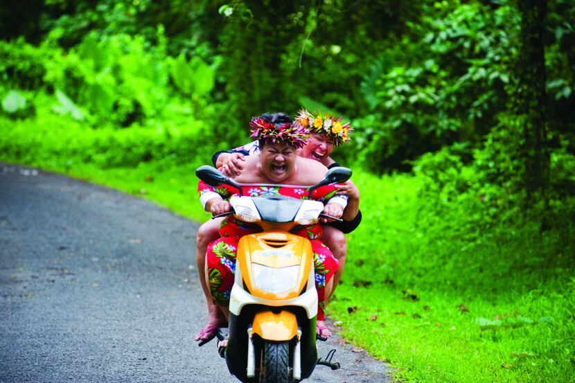 Two local woman share a laugh as they travel along a side road on Rarotonga. Scooters are...