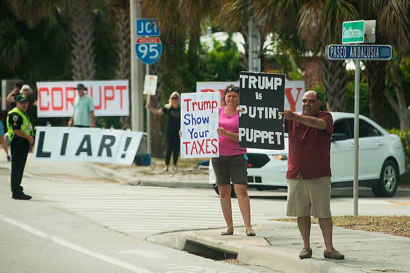 Protesters hold placards as the motorcade of US President Donald Trump passes in West Palm...