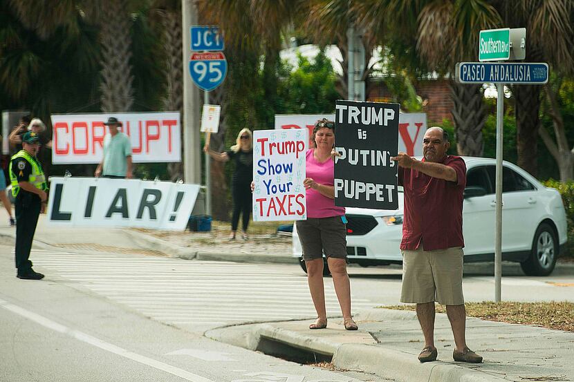 Protesters hold placards as the motorcade of US President Donald Trump passes in West Palm...