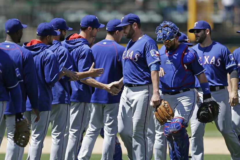 Texas Rangers pitcher Colby Lewis, center, shakes hands with teammates at the end of a...