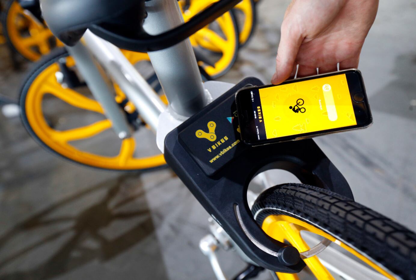 The app on a smartphone is used to unlock a VBike smart lock box on the rear tire of a...