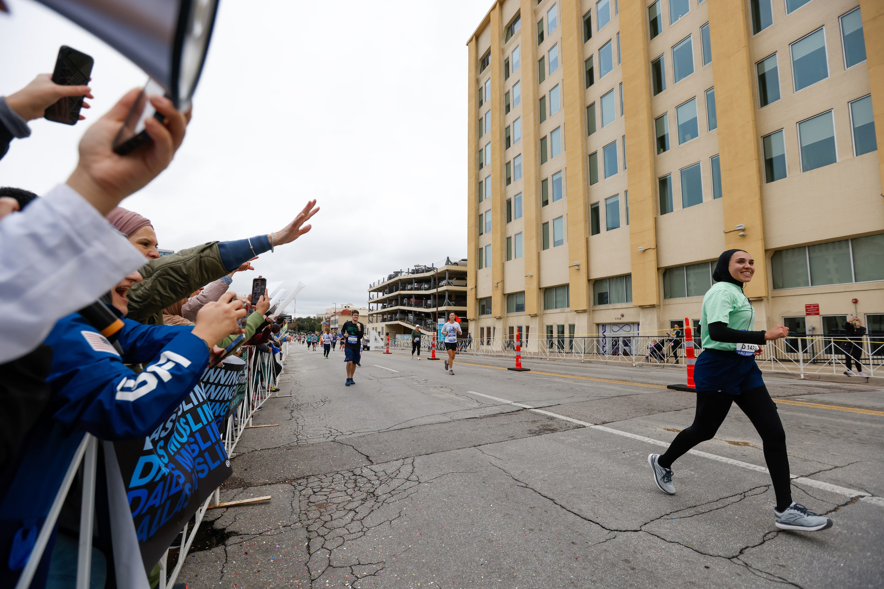 Members and supporters of local running club RunDMRC cheer for member Tala Younis as she...