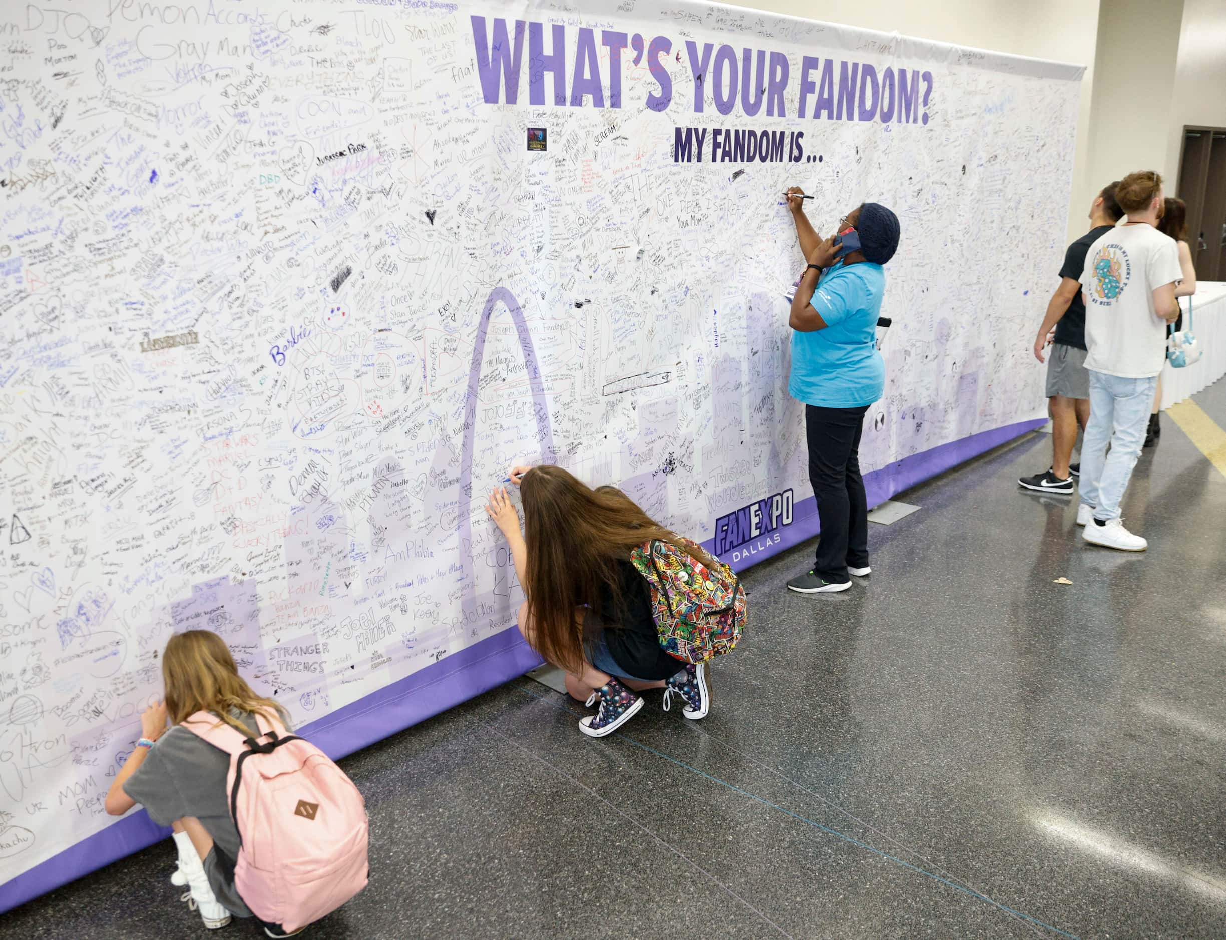 People sign a wall with their fandom at Fan Expo Dallas at the Kay Bailey Hutchison...