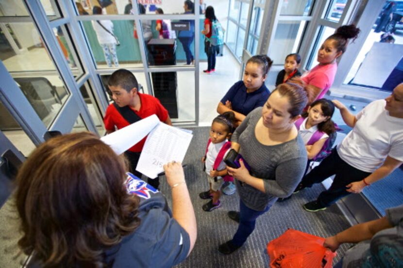 La maestra asistenta dirige a estudiantes y padres de familia durante el primer día de...