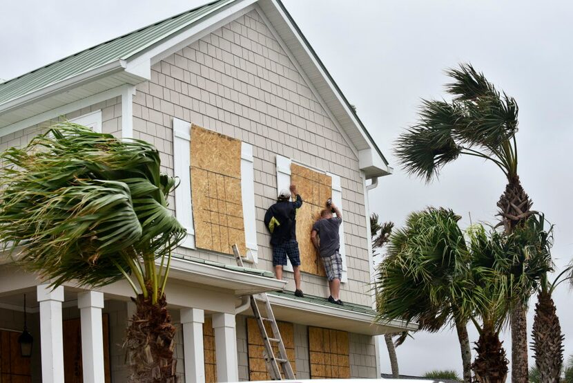 Workers from Armstrong Construction put plywood over windows of a home in preparation for...