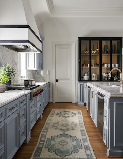 Blue cabinetry in a kitchen, decorative rug runs through the length of the kitchen,...