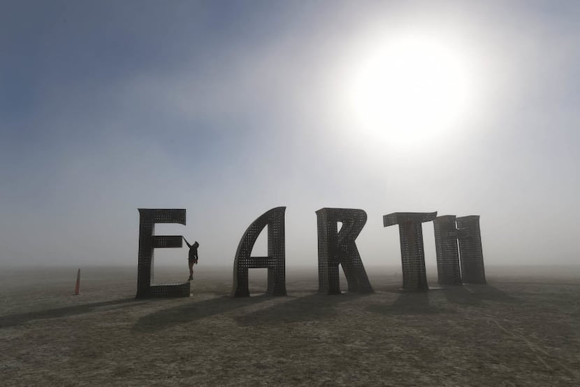 Anita Vranckx, of Belgium, hangs from the E of an Earth sculpture at Burning Man on a dusty...