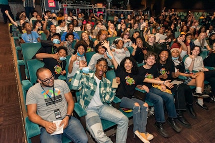 A group of high school students cheering and smiling while sitting in the audience of a...