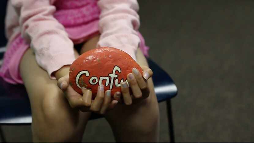 A participant in the Five Star Kids program holds a stone painted with the word "confused"...