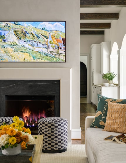 White fireplace with a television above, with wood beams in the adjacent hallway