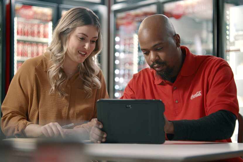 Coca-Cola Southwest Beverages employee in red polo shirt shows woman something on a laptop.