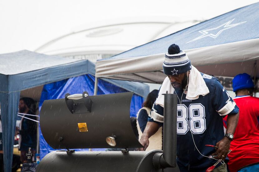 Dallas Cowboys fan Carey Herron mans a grill in the rain while tailgating before an NFL...