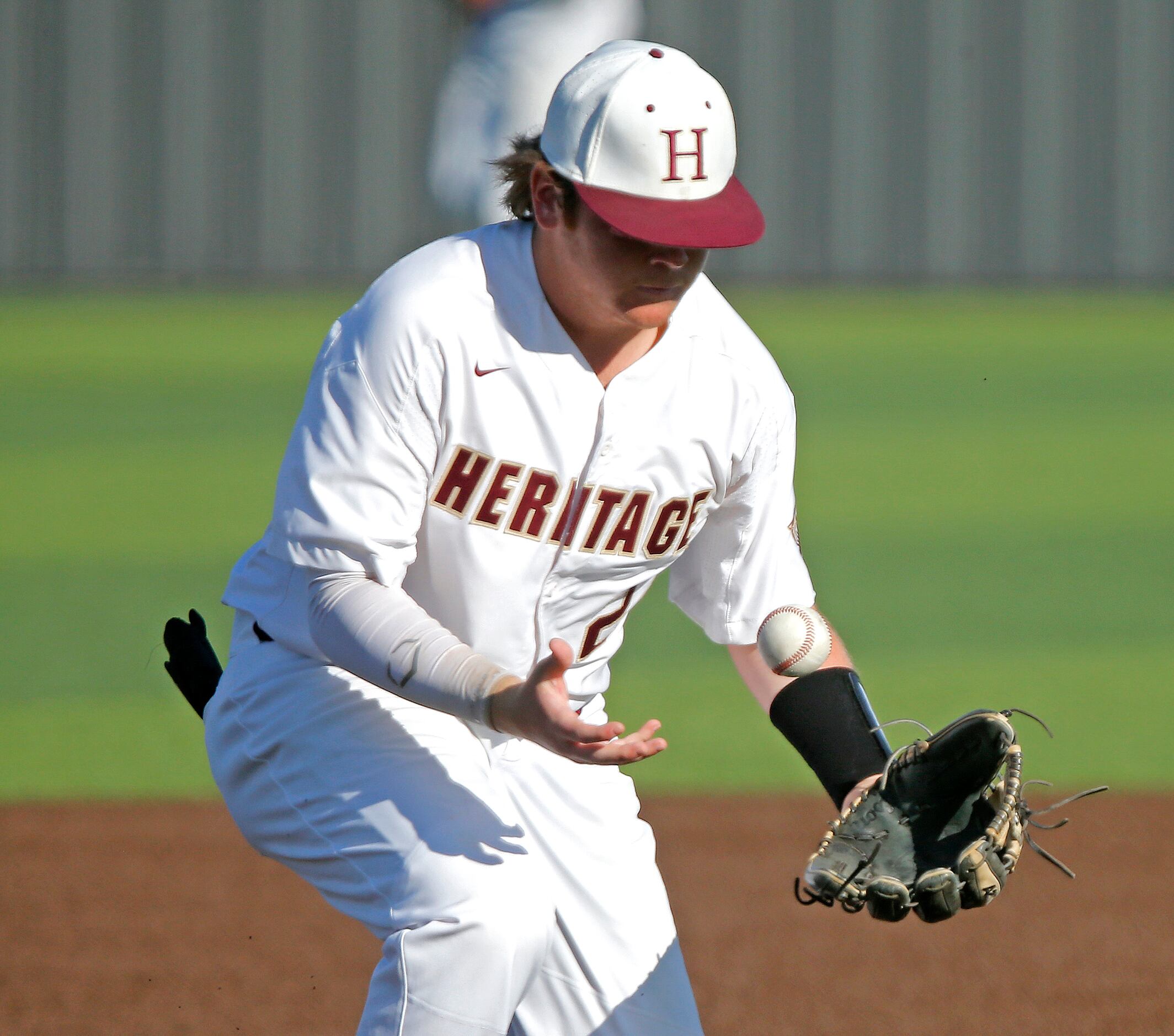 Heritage third baseman Andrew Hickey (24) bobles a hit before making the throw out in the...