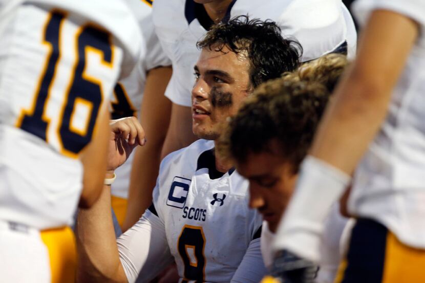 Highland Park QB John Stephen Jones (hand up) talks with teammates on a bench between series...