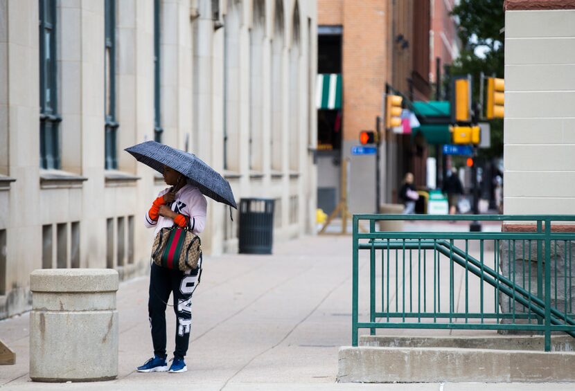 Tina Harris stands under an umbrella as light rain starts to fall outside the County Records...